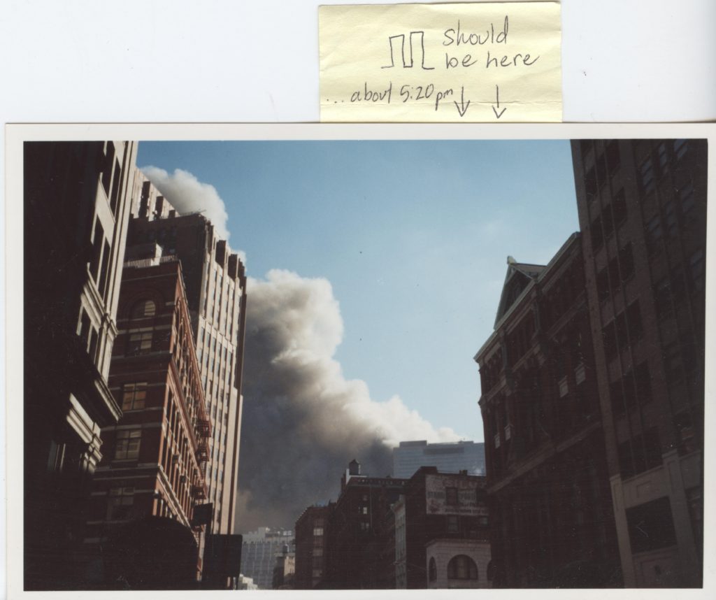 A photo taken in Tribeca looking up at the buildings. There is a large cloud of smoke. A sticky note says "Should be here" with an outline of the two towers and two arrows pointing down. It also says, "about 5:20 p.m."