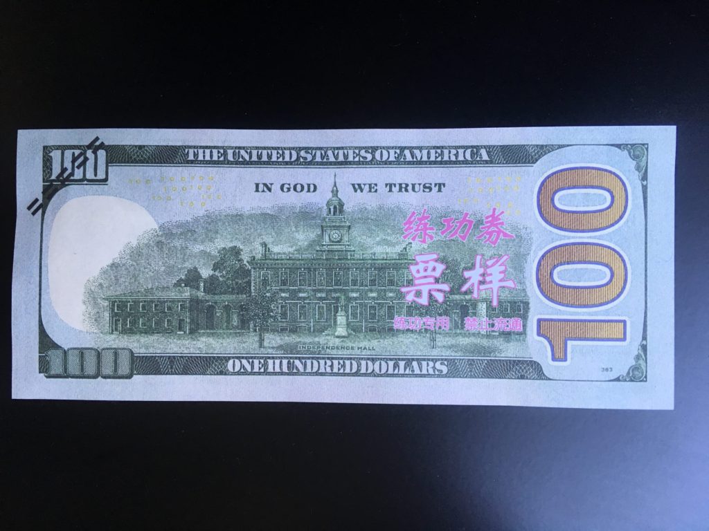 The back of a $100 bill with hot pink Chinese writing.