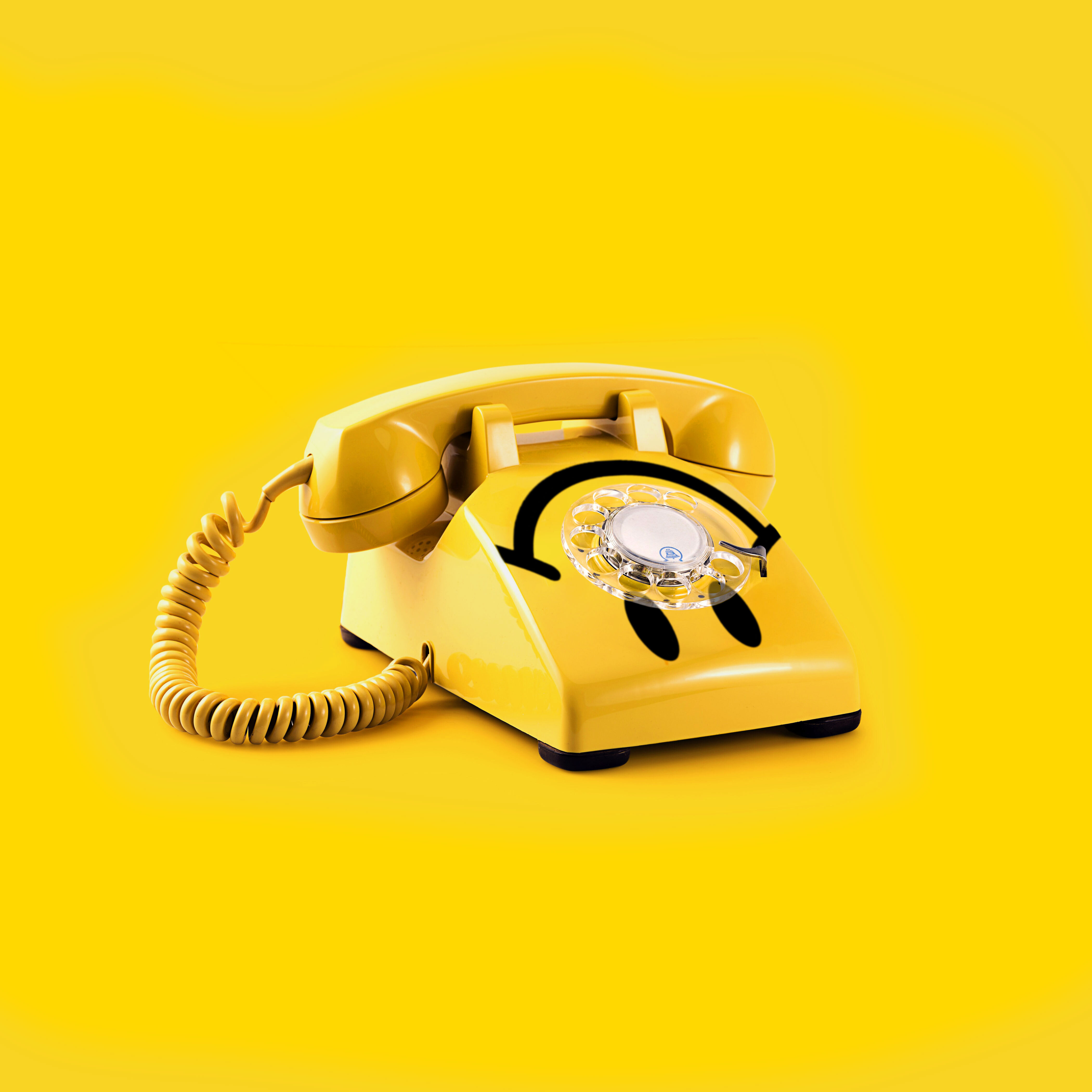 yellow rotary dial phone with underunderstood upside down smiley face on it